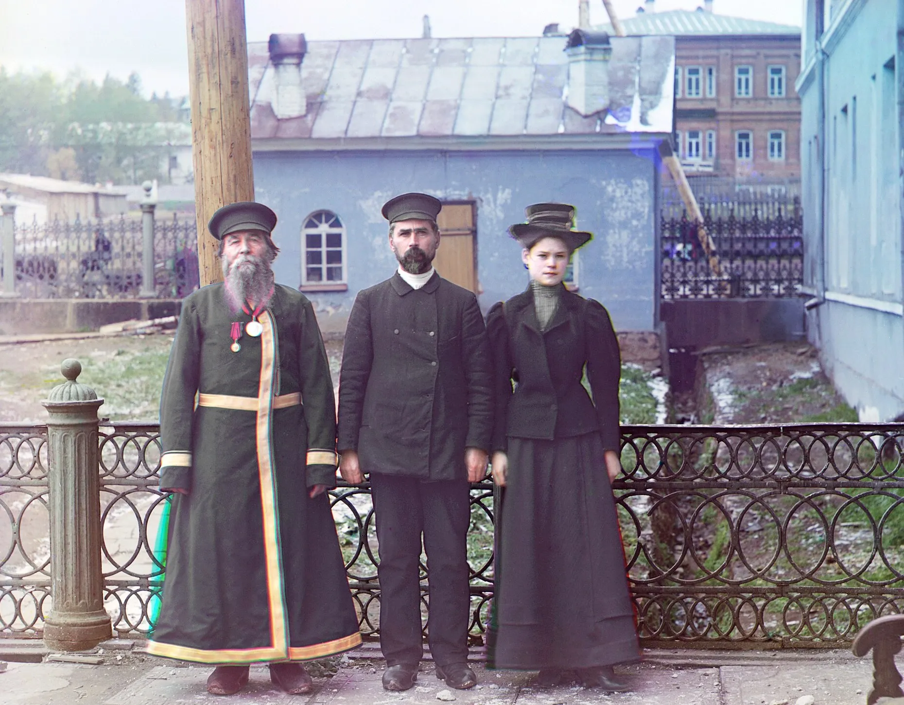Цветная фотография начала XX века: пожилой мастер с окладистой бородой, его сын и внучка у заводского станка
